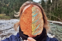 In the GALLERY OF TRAVELING LEAVES Angela Andorrer takes small leaves, which she worked with acrylic, oil, yarn and beads, on hikes and portrays them against landscape backdrops, in widescreen format. She is particularly inspired by leaves having been eaten away by snails, caterpillars, and beetles. When a leaf breaks in a thin place, she sews it back together, much like a surgical operation. Aspects of the cinematic, moving in nature and mindfulness, become part of the work. We must learn again to be respectful of the trees, the plants and the leaves, because nature, forms the climate that surrounds us, which means the basis of our life. Each leaf becomes a 'relic of nature' and a kneel before creation. // In der GALERIE DER REISENDEN BLÄTTER nimmt Angela Andorrer kleine Blätter, die sie mit Acryl, Öl, Garn und Perlen bearbeitete, mit auf Wanderungen und porträtiert sie vor Landschaftskulissen, im Breitbildformat. Besonders inspirieren sie von Schnecken, Raupen und Käfern zerfressene Blätter und wenn ein Blatt an einer dünnen Stelle bricht, näht sie es wieder zusammen, ähnlich einer chirurgischen Operation. Aspekte des Filmischen, das in der Natur Bewegen, die Achtsamkeit, werden zum Teil der Arbeit. Wir müssen wieder lernen respektvoll mit den Bäumen, den Pflanzen und den Blättern um zu gehen, denn die Natur, bildet das Klima, das uns umgibt und das unsere Lebensgrundlage bildet. Jedes Blatt wird zur ‚Reliquie der Natur‘ und zum Kniefall vor der Schöpfung.